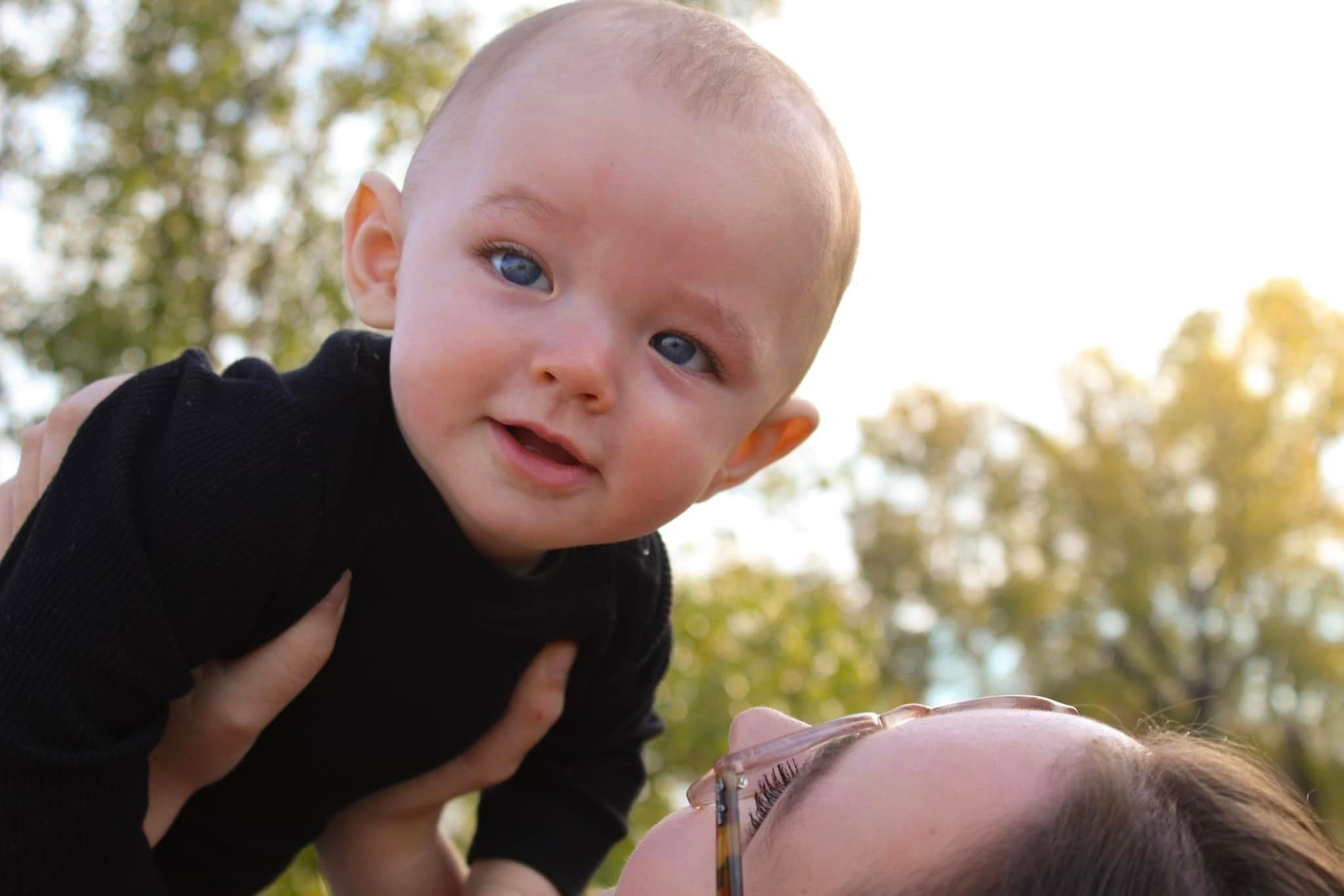 Baby being lifted into the air, smiling at the camera