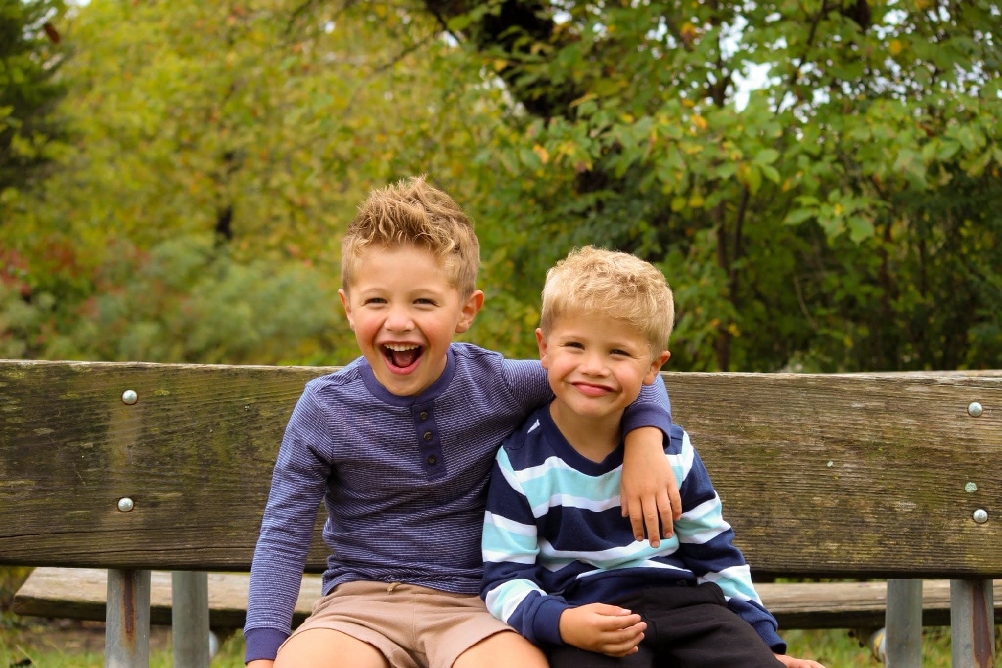 Two brothers laughing with arms around each other on a bench